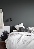 Teller mit Plätzchen auf Bett mit weißer Bettwäsche, daneben Leselampe an grauer Wand und schwarz-weiße Fotografie