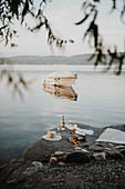 Bottle of sparkling wine, glasses, sunhat, sandals and blanket on rocky lake shore