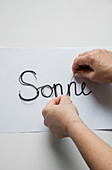 Hands bending wire to make the word 'Sonne' (sun)