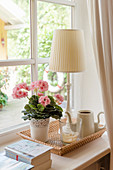 Table lamp, potted geranium and teapot on cork tray on windowsill