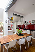 White chairs around dining table in open-plan kitchen with red splashback