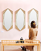 Woman sitting on bench in front of three mirrors on pink wall