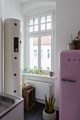Pink fridge next to window and round cabinet in kitchen