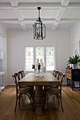 Solid wooden dining table in elegant, white interior with coffered ceiling