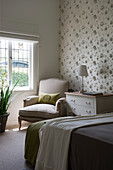 Antique armchair and white chest of drawers against floral wallpaper