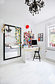 Desk and large black-framed mirror in teenager's bedroom decorated in white