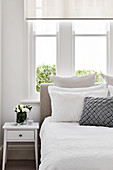 Bed below window in bright bedroom decorated in white and grey