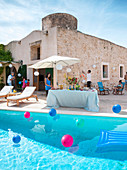Party buffet under parasol next to colourful balloons floating in sunny swimming pool