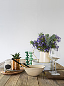 Simple kitchen utensils and jug of flowers on wooden table