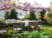 Crockery on tables in garden below pink-flowering wisteria