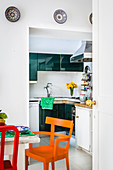 Dining table and colourful chairs next to open doorway leading into kitchen