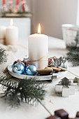 Lit candle on metal plate, pastry cutters and blue baubles