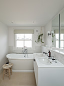 White bathroom with twin washstand and bathtub below lattice window