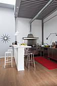 Open-plan stainless steel kitchen with white breakfast bar and steel ceiling in loft apartment