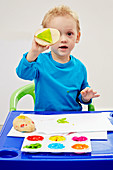Kleiner Junge macht mit bunten Fingerfarben Kartoffeldruck