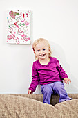 Little girl sitting on sofa back below her painting on wall
