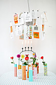 Designerleuchte mit Postkarten über bunten Vasen mit einzelnen Blumen
