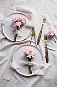 Kleine Sträußchen aus rosafarbenen Nelken mit Stoffbändern auf Tellern