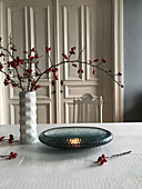 Glass bowl and branches of rose hips on table in front of antique wooden door