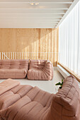 Modular seating area in pastel colors with wood-paneled wall and white curtain