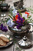 Colourful bouquet of sweet peas and green asparagus in old silver teapot and plate of biscuits