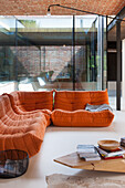 Wohnzimmer mit orangefarbener Ledercouch und Holztisch vor Glasfront