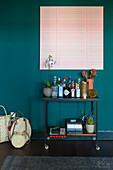Bar trolley with spirits in front of dark green wall with pink artwork