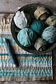 Strips of fabric in shades of blue and green with spools of thread and bowl full of fabric balls