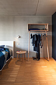 Minimalistisches Schlafzimmer mit Holzkleiderständer, Beistelltisch und Betonwand