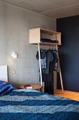 Moderne Garderobe aus Holz im Schlafzimmer mit Betonwand und blauer Bettwäsche