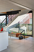 Modern staircase with glass banister with bench under stairs; white kitchen island