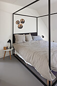 Minimalistisches Schlafzimmer mit schwarzem Himmelbett und grauer Bettwäsche