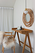 Holzkonsole und Stuhl mit Felldecke, runder Bambus-Spiegel an weißer Wand