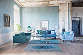 Sofas in shades of blue in living room of period building with distressed walls and ceilings