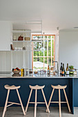 Three-legged barstools at blue kitchen counter in open-plan kitchen