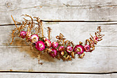 Kleine Girlande mit Strohblumen-Blüten auf getrocknetem Farnblatt
