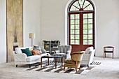 Various upholstered furnishings on striped rug in front of arched window