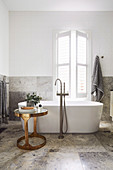Freistehende Badewanne und goldener Beistelltisch vorm Fenster