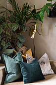 Cushions in petrol-blue, silver and ochre in front of houseplants