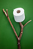 Branch used as toilet roll holder against green wall