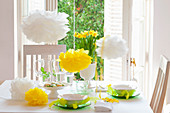 Easter table set in spring colours with paper flowers, feathers and narcissus
