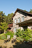 Liegestühle auf der Terrasse im Garten vorm rustikalen Holzhaus