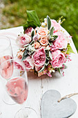Lavish bouquet of roses, lily-of-the-valley and lamb's ear, glasses of pink Champagne and heart pendant