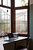 Arbeitsplatz mit Laptop am Fenster mit Blick auf Gewächshaus