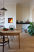Wooden table and rattan chairs in dining room with fireplace and houseplant