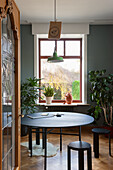 Round dining table with green pendant light and houseplants in front of the window