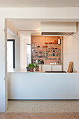 Open-plan kitchen with bar counter and shelves full of spices and glassware