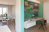 Home office with wall shelves on a mint green wall with a view into the dining area