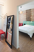Bedroom with brick wall, bed with geometrically patterned headboard and standing mirror