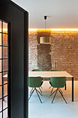 Essbereich mit grünen Stühlen, Backsteinwand und indirekter Beleuchtung